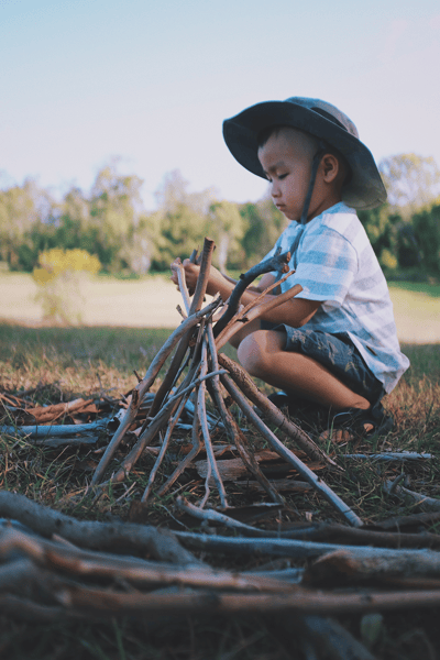 young boy building campfire with sticks outdoors camping